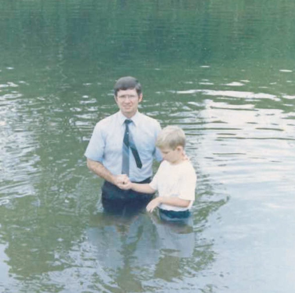 Steve baptizing a young boy in a river